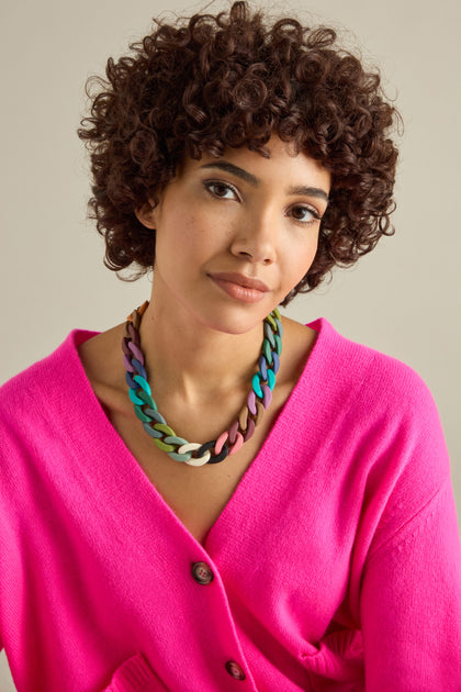 A person with curly hair wears the vibrant Colour Pop Link Necklace, a statement piece that perfectly complements their bright pink cardigan.