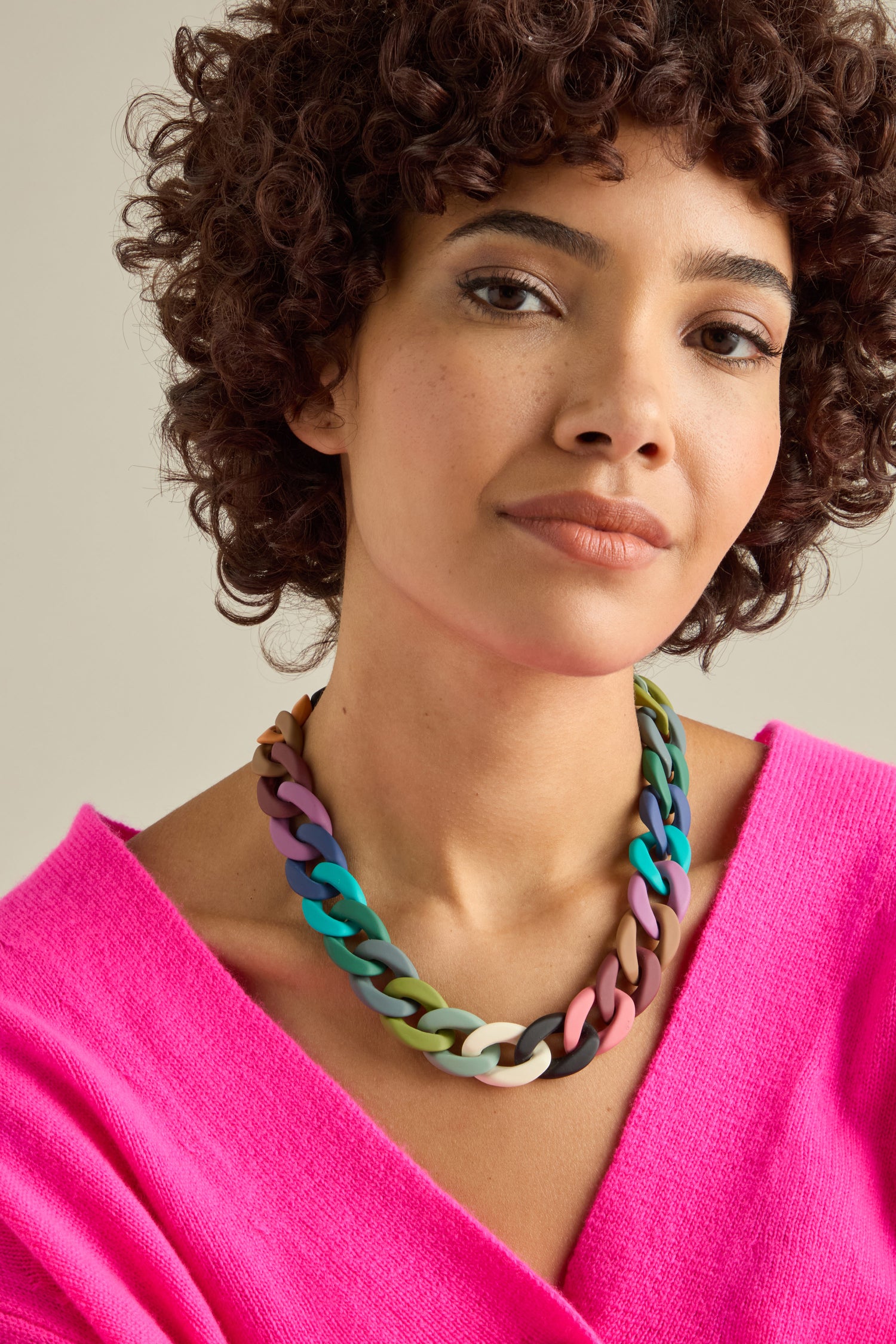 A person with curly hair wears a bright pink top and a bold Colour Pop Link Necklace as the statement piece, looking confidently at the camera.