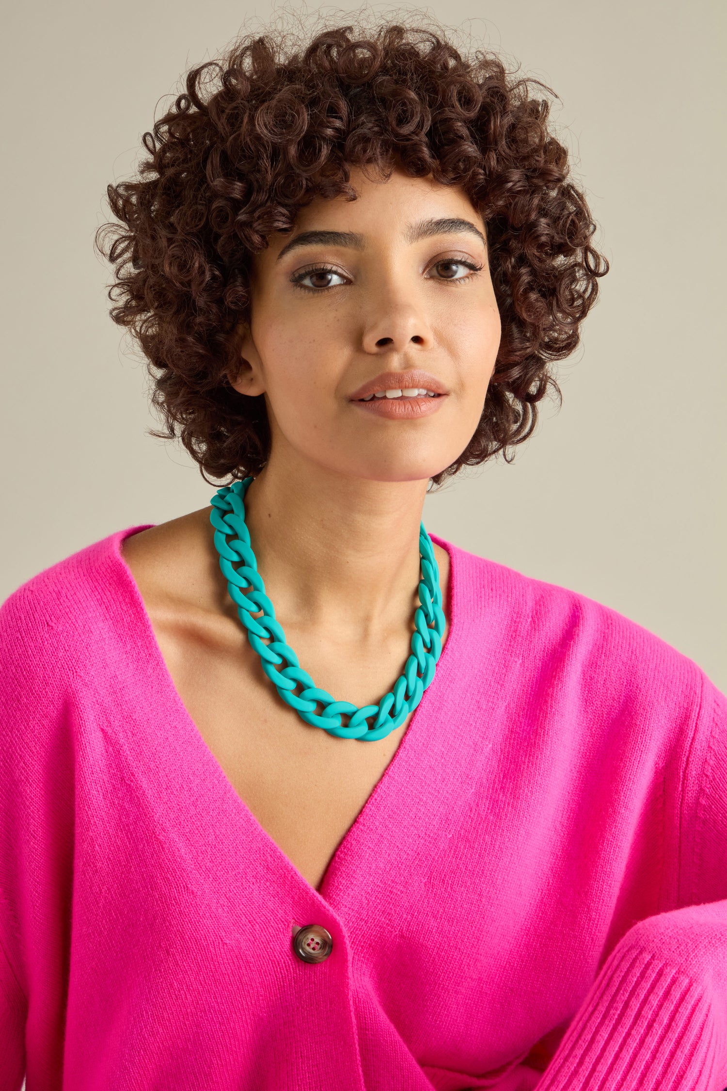 A person with curly hair wearing a bright pink cardigan and the Colour Pop Link Necklace, creating a perfect statement piece against a neutral background.