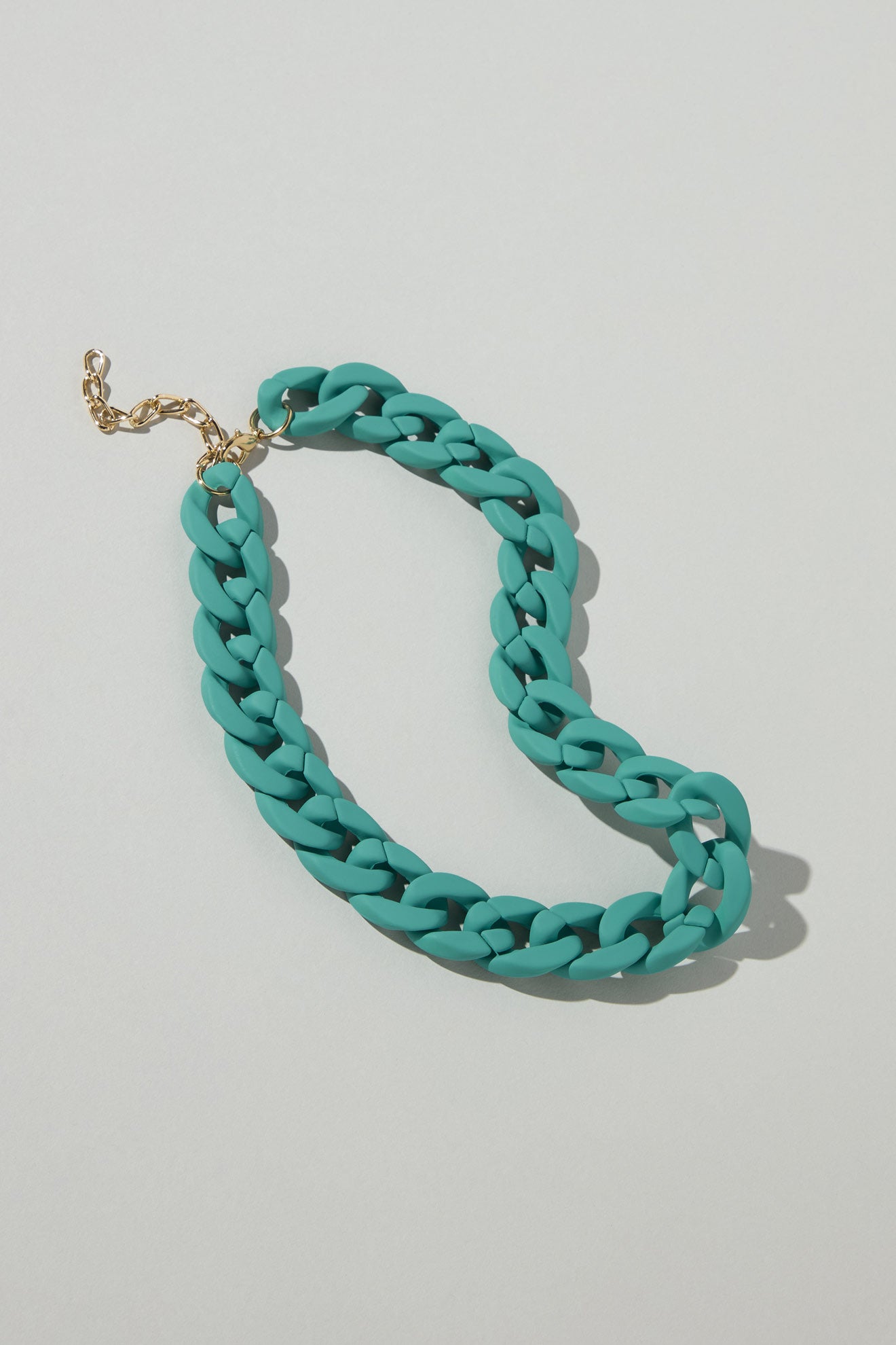 The Colour Pop Link Necklace, featuring a teal chain and gold clasp, is displayed on a plain light background as a striking statement piece.