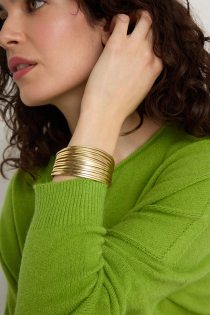 A woman wearing a green sweater pairs it with a Vegan Leather Metallic Bracelet.
