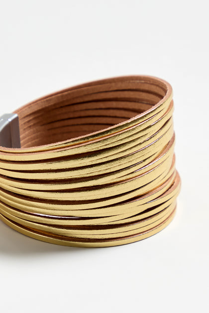 The Vegan Leather Metallic Bracelet boasts multiple slim metallic gold bands wrapped around wide brown vegan leather, creating a striking yet lightweight accessory.