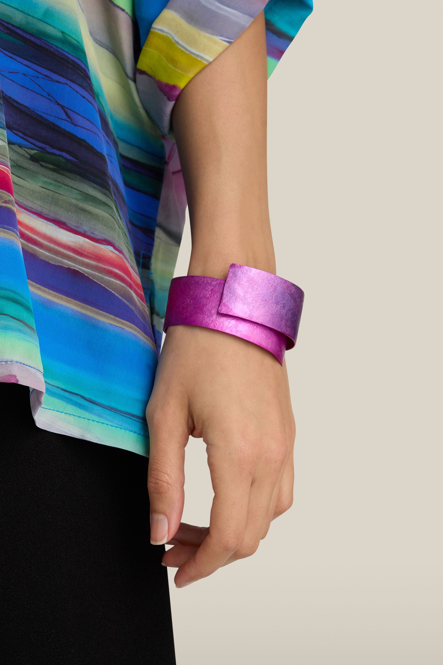 A person wearing a colorful striped shirt and black pants, with a large magenta handcrafted Curved Bracelet on their left wrist.