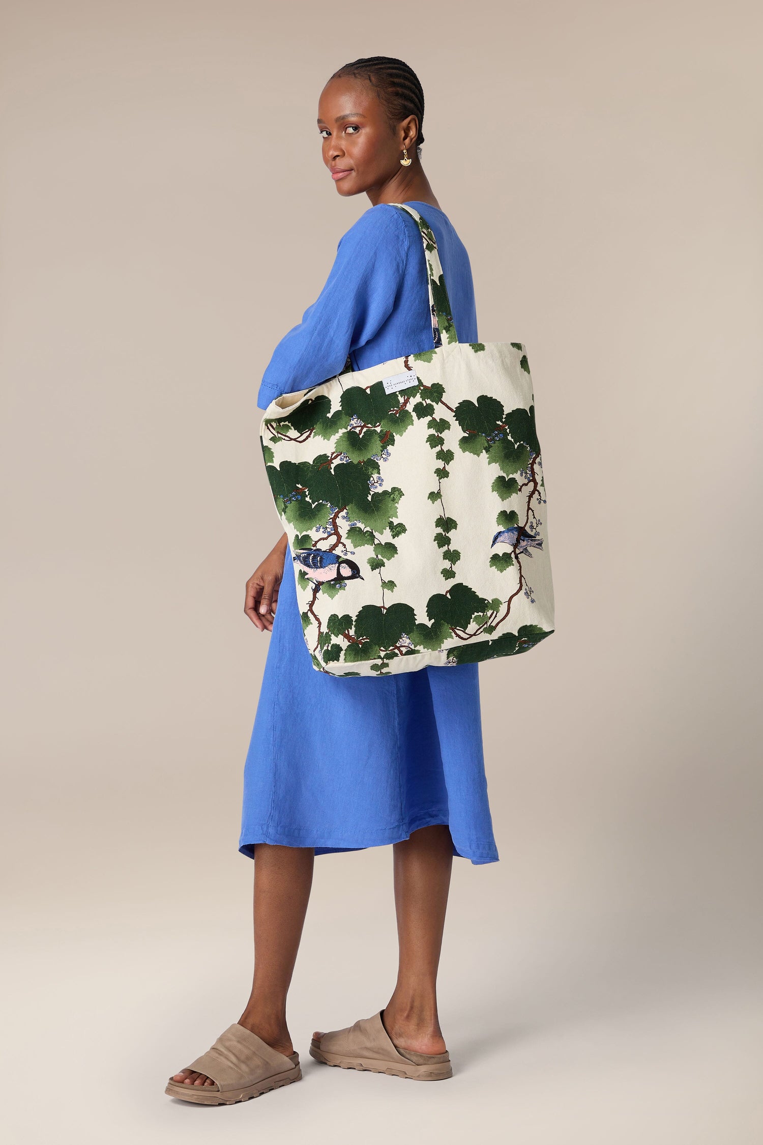 Woman in a blue dress holding a large floral-patterned, sustainable cotton Acer Canvas Bag.