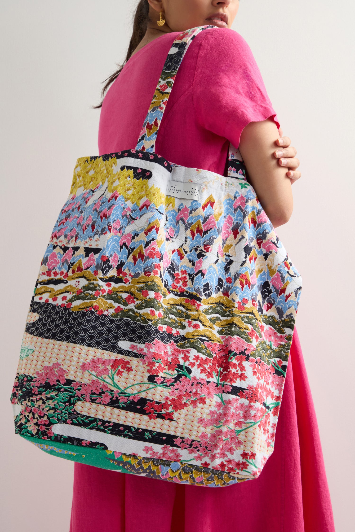 A person in a pink dress holds the Spring Print Canvas Bag, a large tote made from sustainable cotton, elegantly slung over their shoulder.