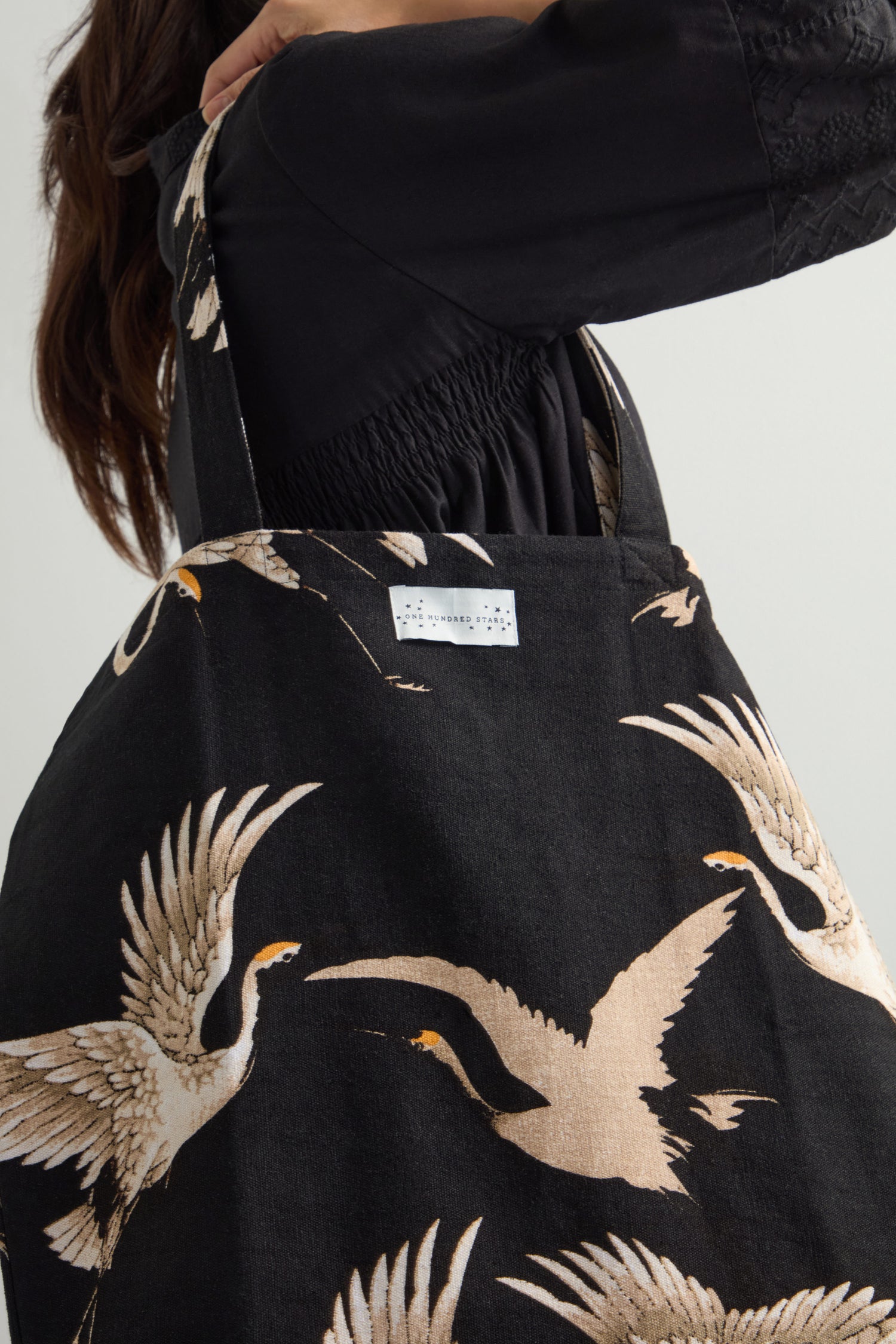 A person wearing a black top holds a Stork Canvas Bag made of sustainable cotton with a crane pattern.