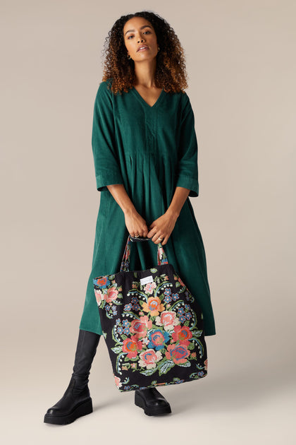 An elegant woman in a sustainable cotton green dress carrying a Woven Flower Canvas Bag.