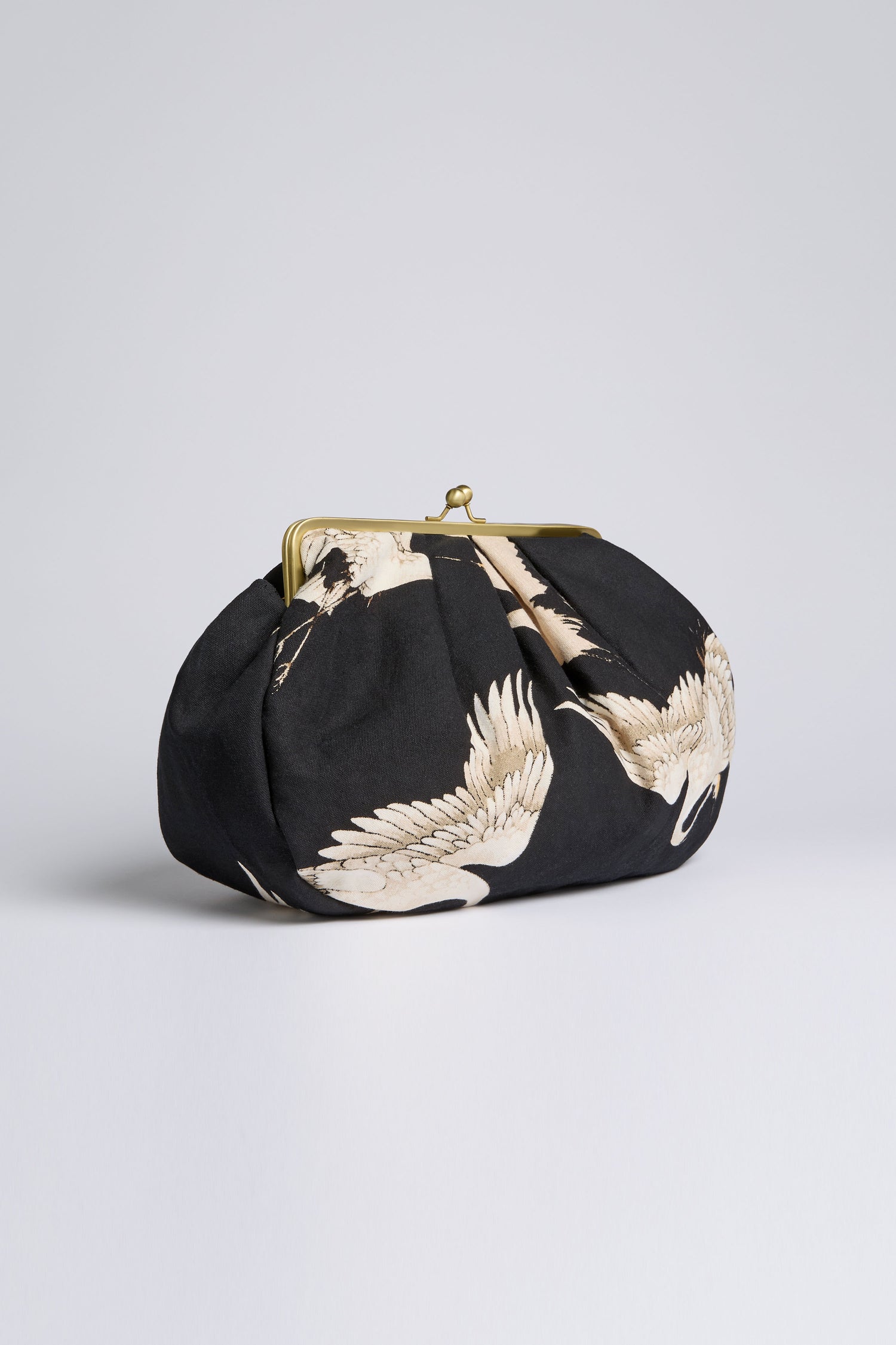 The Stork Print Clasp Bag, made from black organic cotton and featuring a bold stork design with a metal clasp, adds art deco flair as it rests elegantly on a plain surface against a light background.