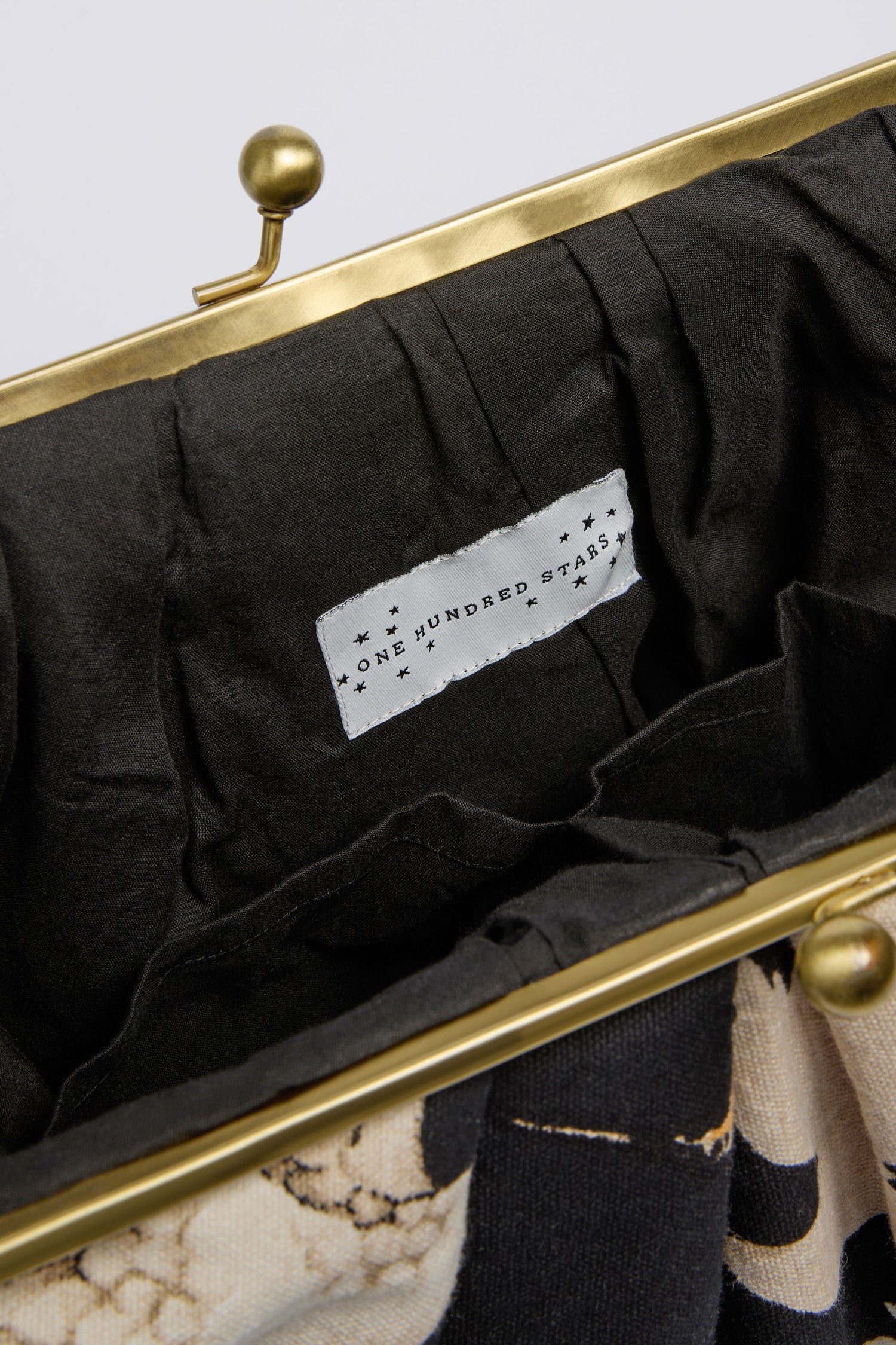 Close-up of the Stork Print Clasp Bag’s brass frame and art deco-inspired "One Hundred Stars" label sewn onto its black organic cotton lining.