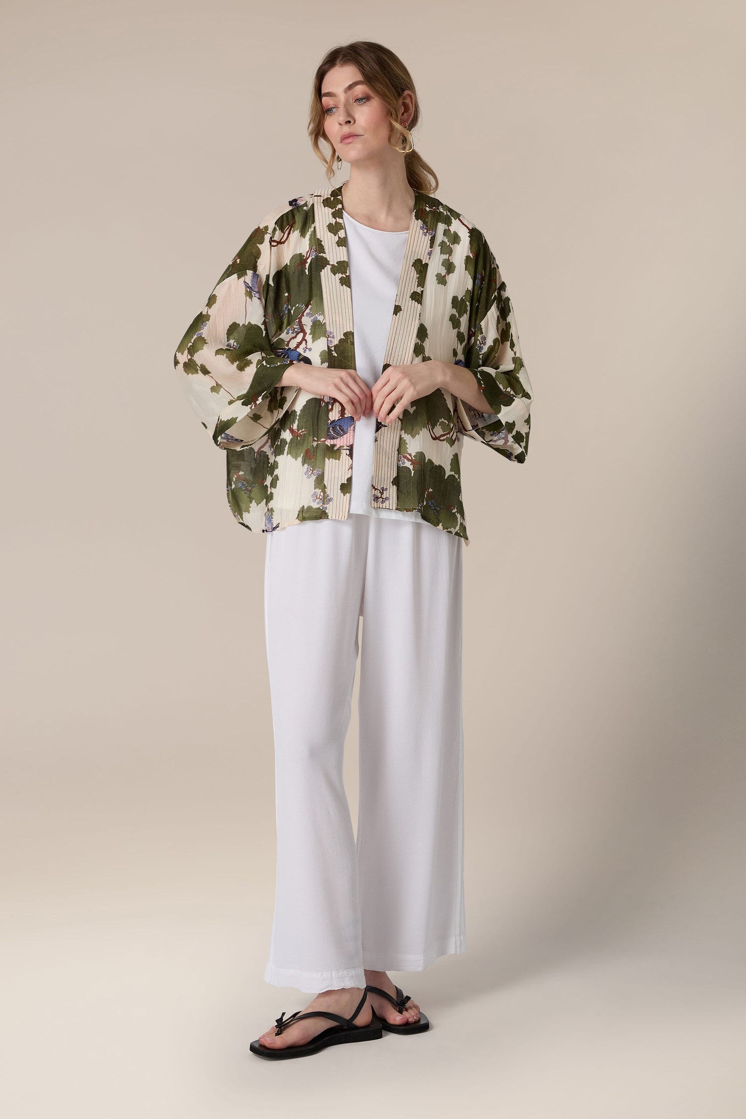 A woman models a spring outfit featuring a camouflaged patterned jacket over a white top paired with white trousers and black sandals, accented by Luxe design elements resembling the Acer Kimono.