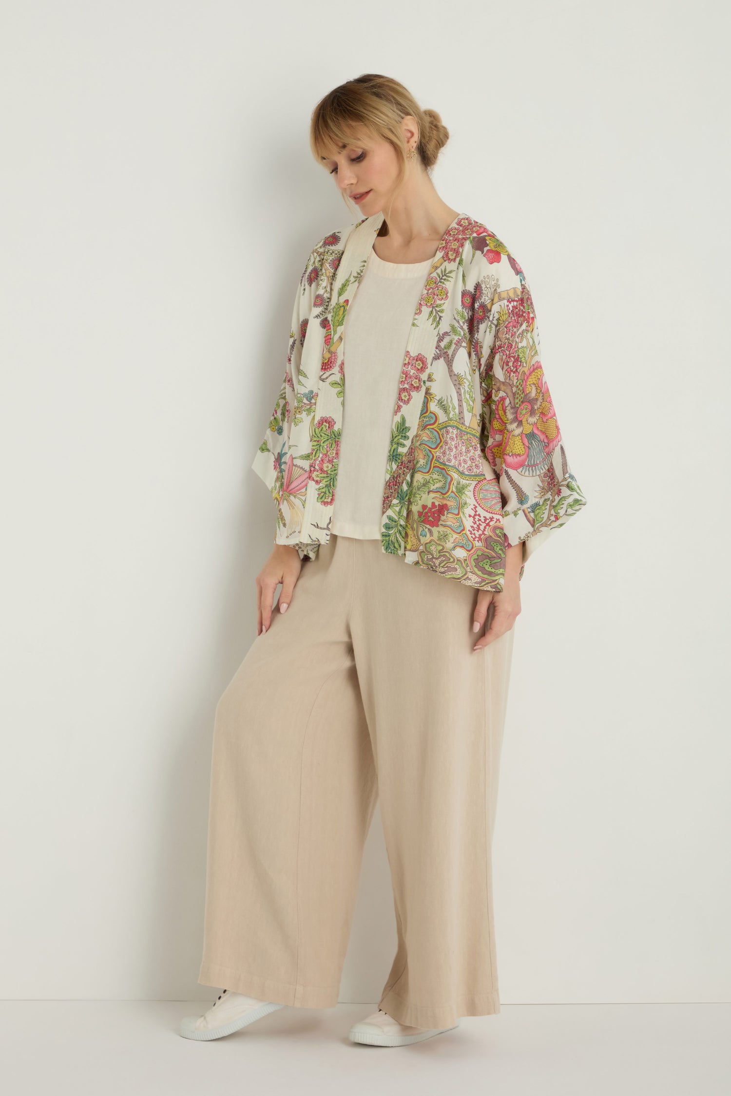 A woman stands against a plain white background wearing a Boho Garden Ecru Print Kimono over a white top and wide-leg beige pants.