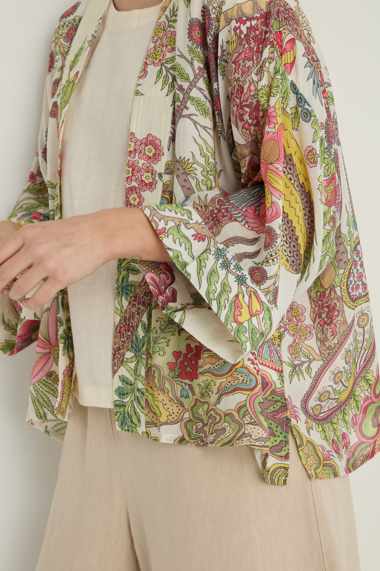 A person wears a Boho Garden Ecru Print Kimono featuring a colorful floral pattern over a beige top and matching pants, shown from shoulders to mid-thigh.