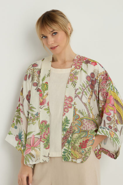 A woman stands against a plain background wearing a Boho Garden Ecru Print Kimono over a cream top and beige skirt.