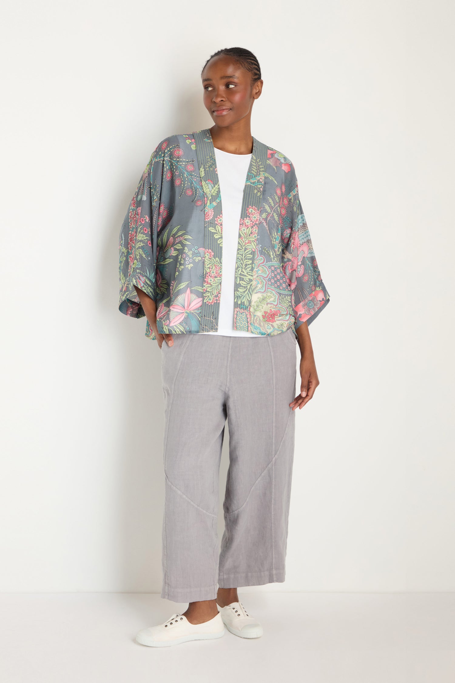 A person stands against a white background wearing the Boho Garden Slate Print Kimono, paired with a white shirt, light gray wide-leg pants, and white sneakers.