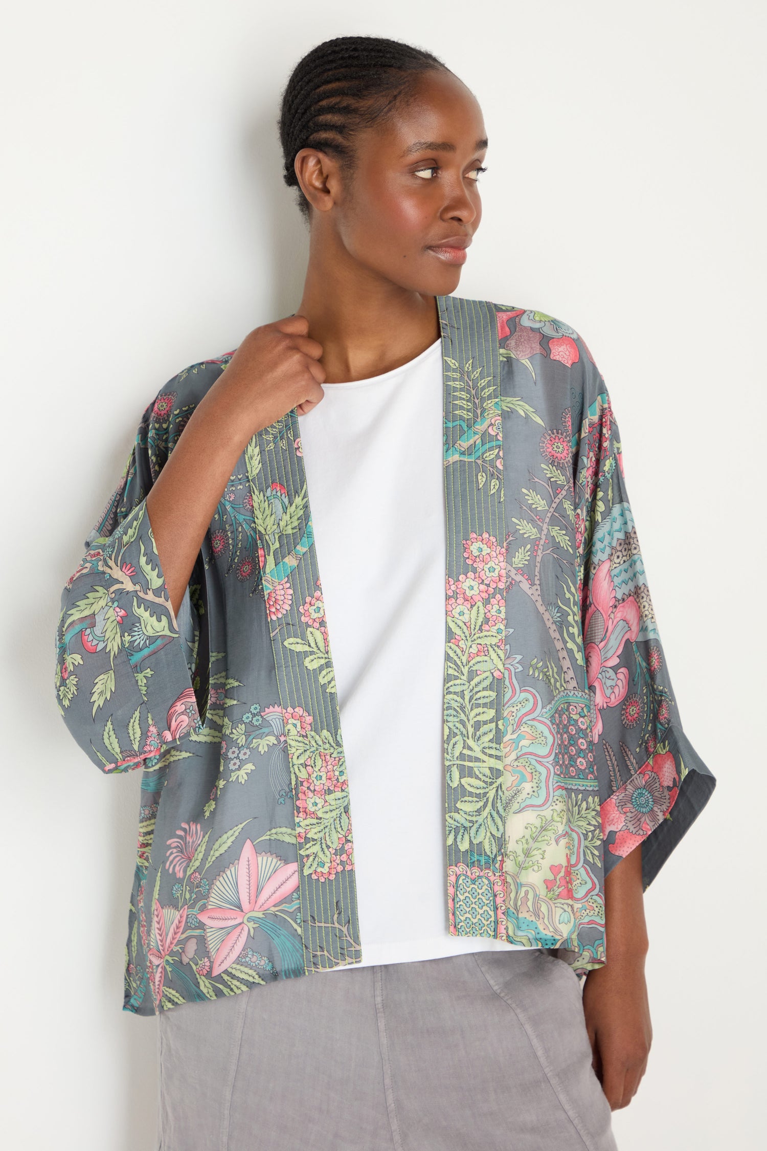 A woman in a Boho Garden Slate Print Kimono with a grey floral design over a white top and grey skirt stands against a plain background.