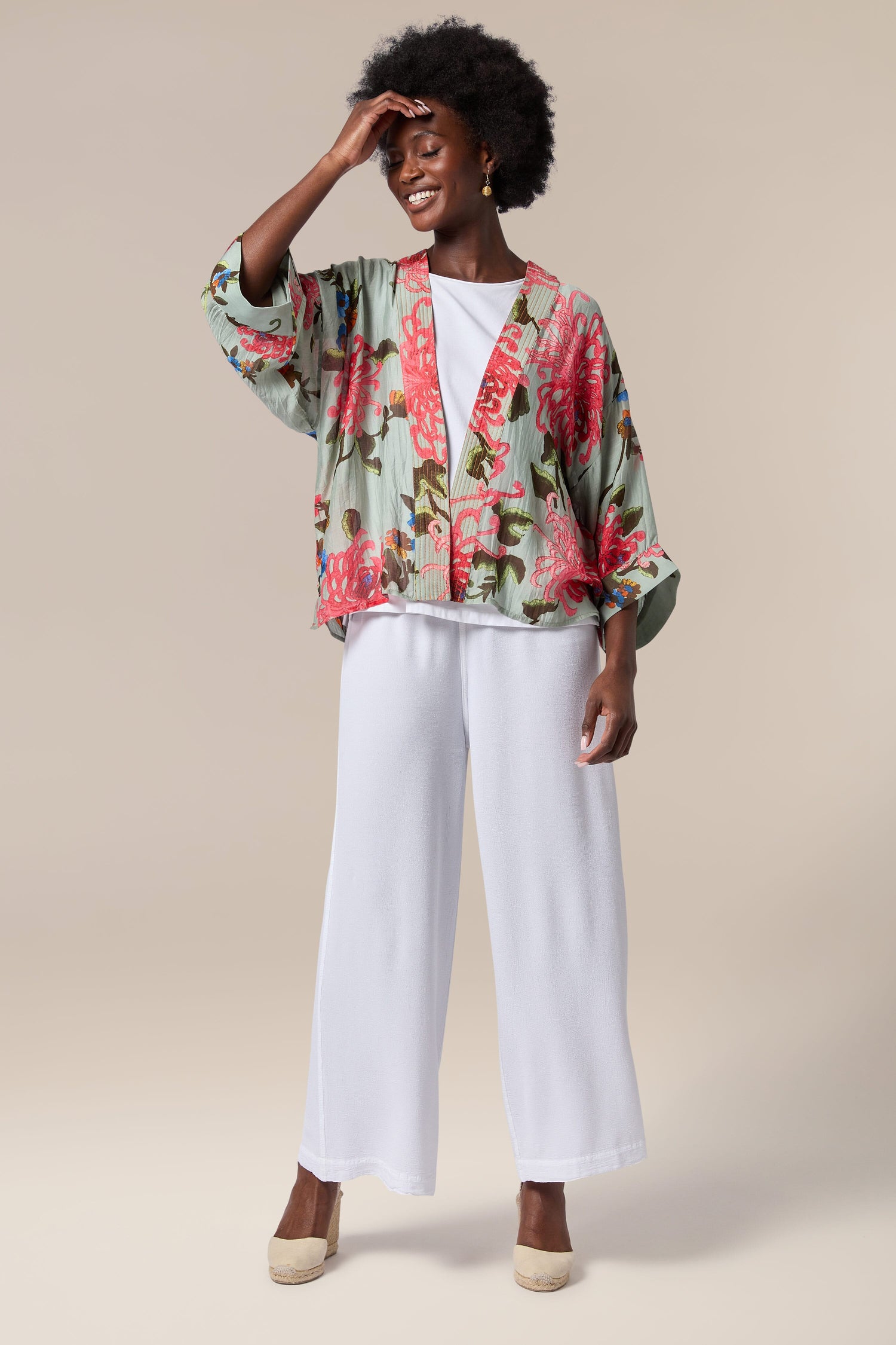 A black woman donning a Chrysanthemum Kimono, a lightweight floral kimono with an open front, paired with white wide leg pants.