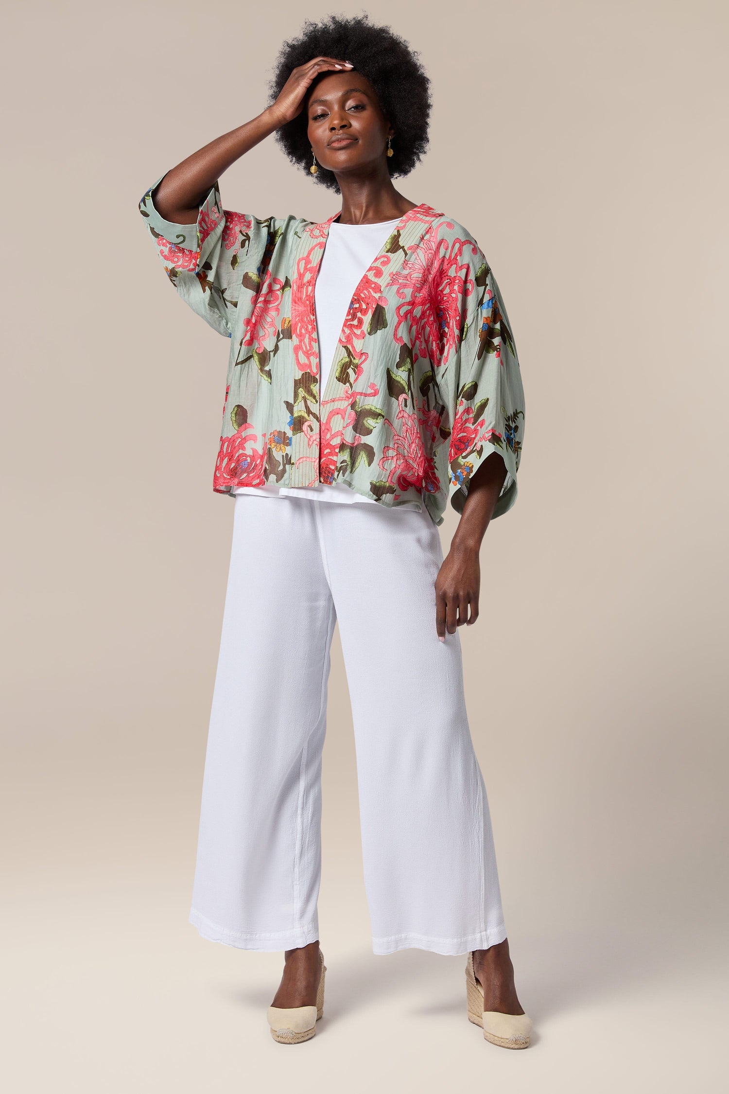 A black woman wearing a Chrysanthemum Kimono jacket and white wide leg pants.