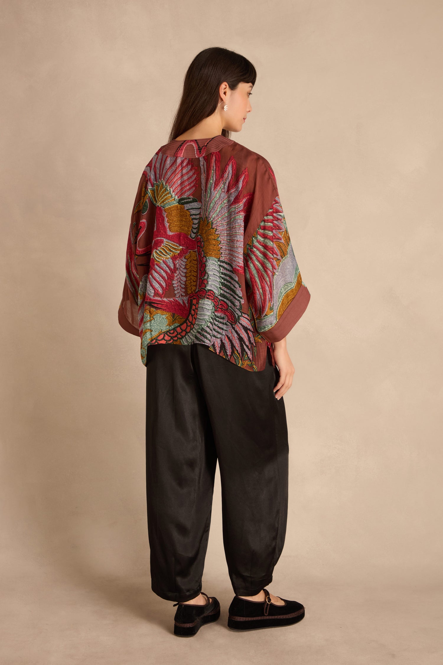 Woman in a Crane Kimono featuring a large crane design on the back and wide black pants, standing sideways against a neutral background.