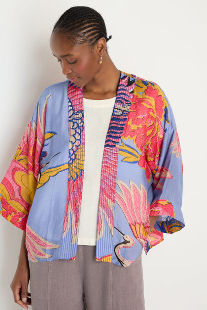 A person wears a Crane Slate Print Kimono in light blue with a vibrant floral pattern over a white top and gray pants, standing against a plain white background.
