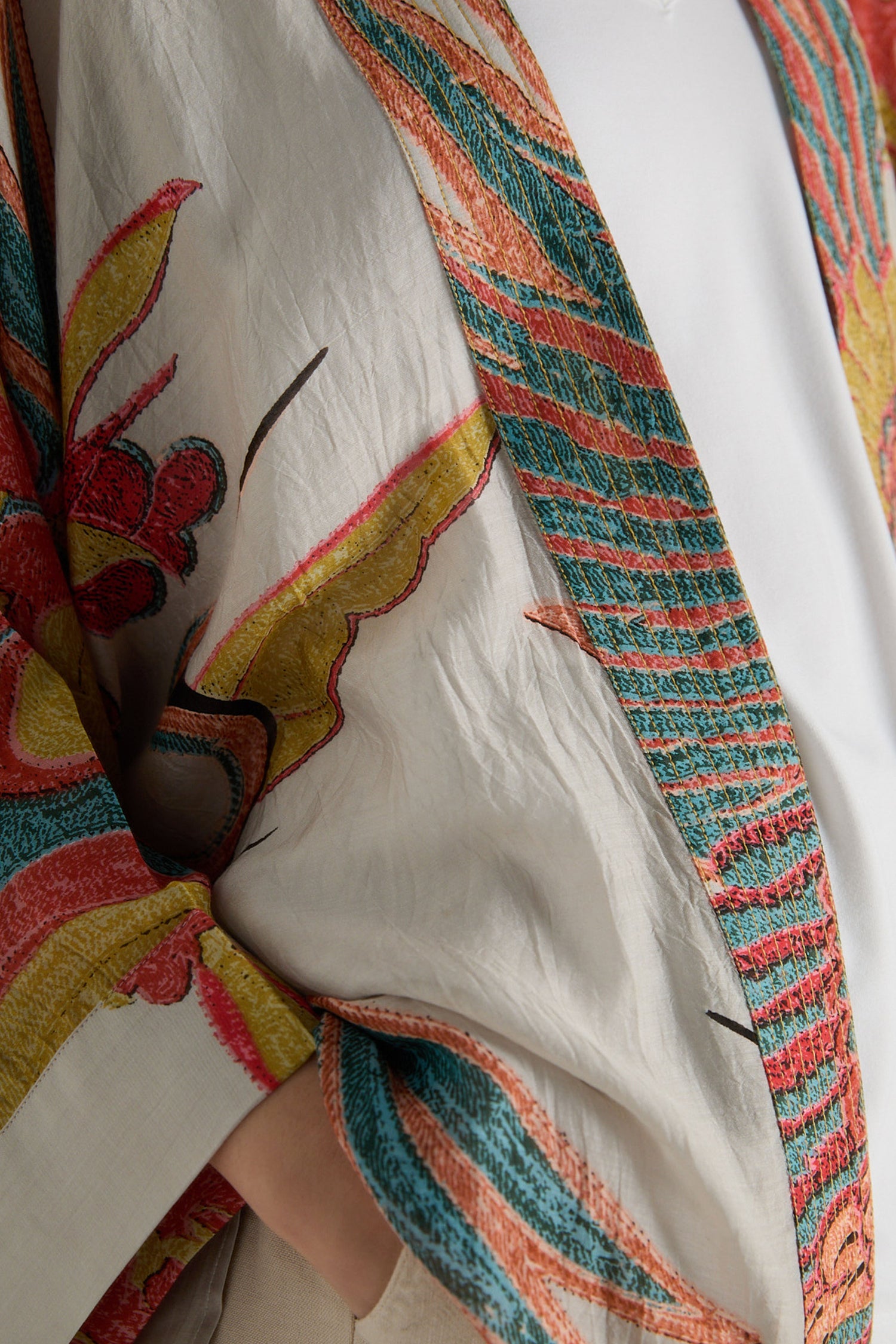 A close-up of a person wearing the Crane Stone Print Kimono, featuring colorful embroidered patterns in red, yellow, and teal on the sleeve and lapel.