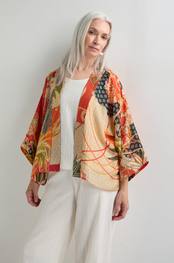 A woman with long gray hair wears the Fans Print Kimono over a white textured outfit, standing against a plain white wall.