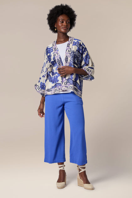 A woman wearing a lightweight blue Willow Kimono jacket with a stunning print, paired with stylish blue culottes.