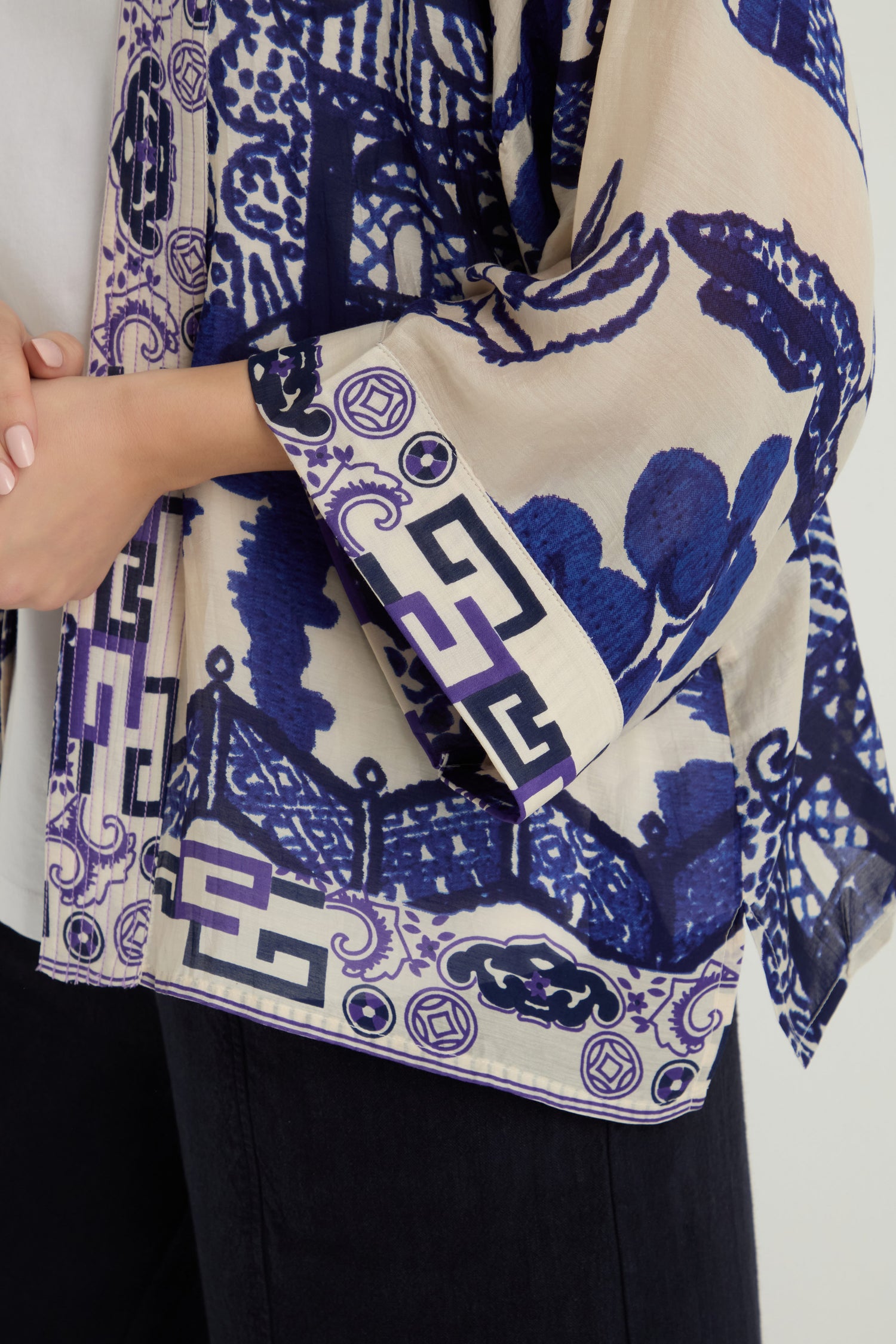 A person wears the Willow Print Kimono—a sheer blue-and-white piece with blue and purple geometric and floral patterns—over a white top and black pants. Only the torso and arms are visible.