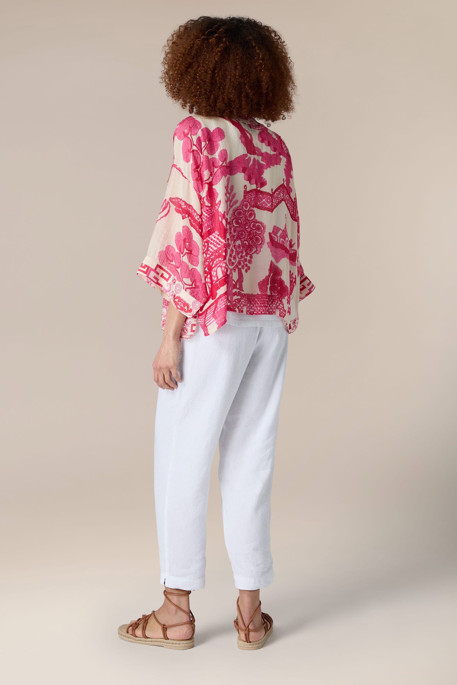 The woman is seen from the back, dressed in a pink Willow Kimono with delicate willow print, paired with white pants.