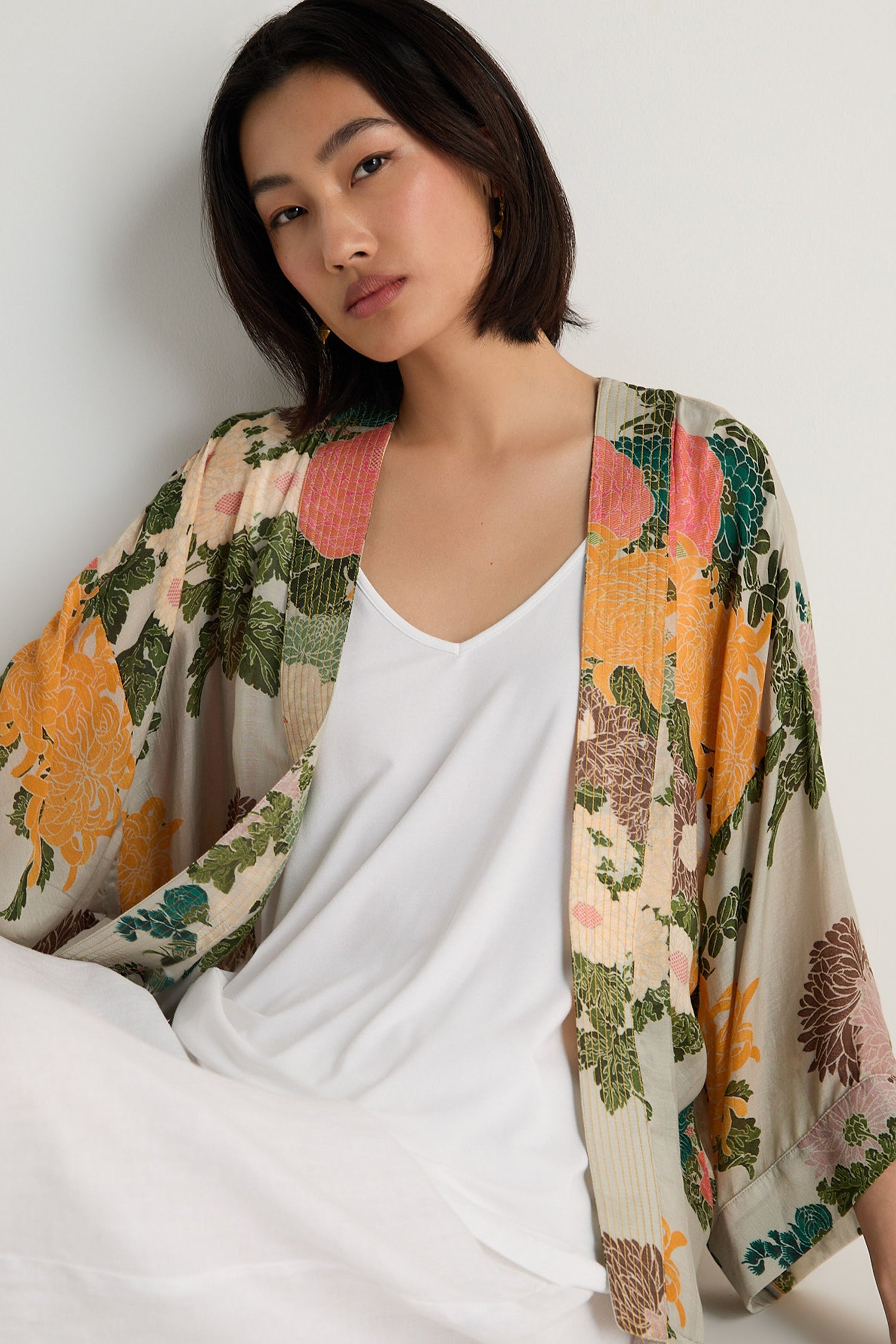 A woman with a straight bob wears a white top and the Jacquard Kimono, featuring a floral print and crafted from a soft modal cupro blend, as she poses against a plain light background.