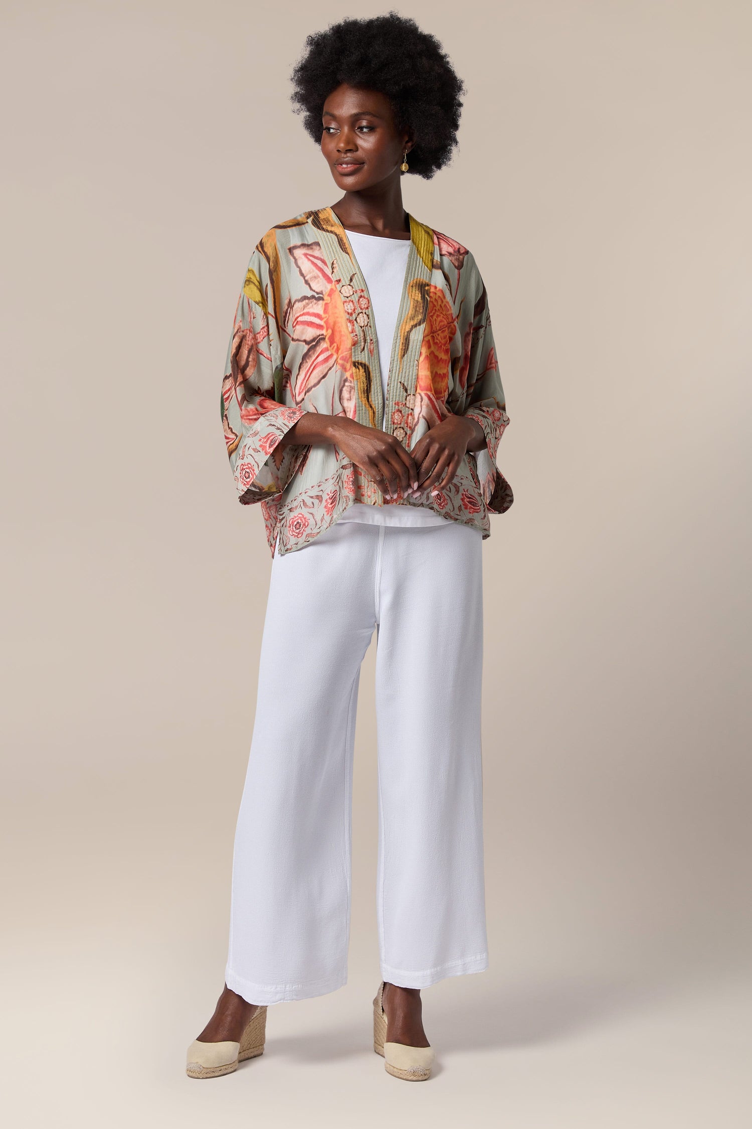 A woman wearing lightweight white pants and a floral print Joy Kimono by One Hundred Stars.