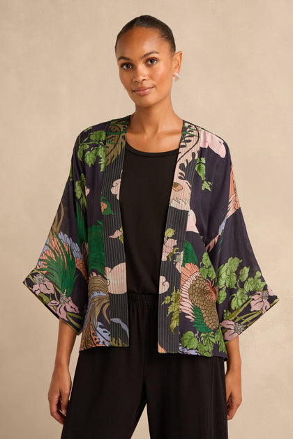 A woman models the Phoenix Kimono, a dark floral kimono-style jacket, layered over a black top and pants against a neutral background.