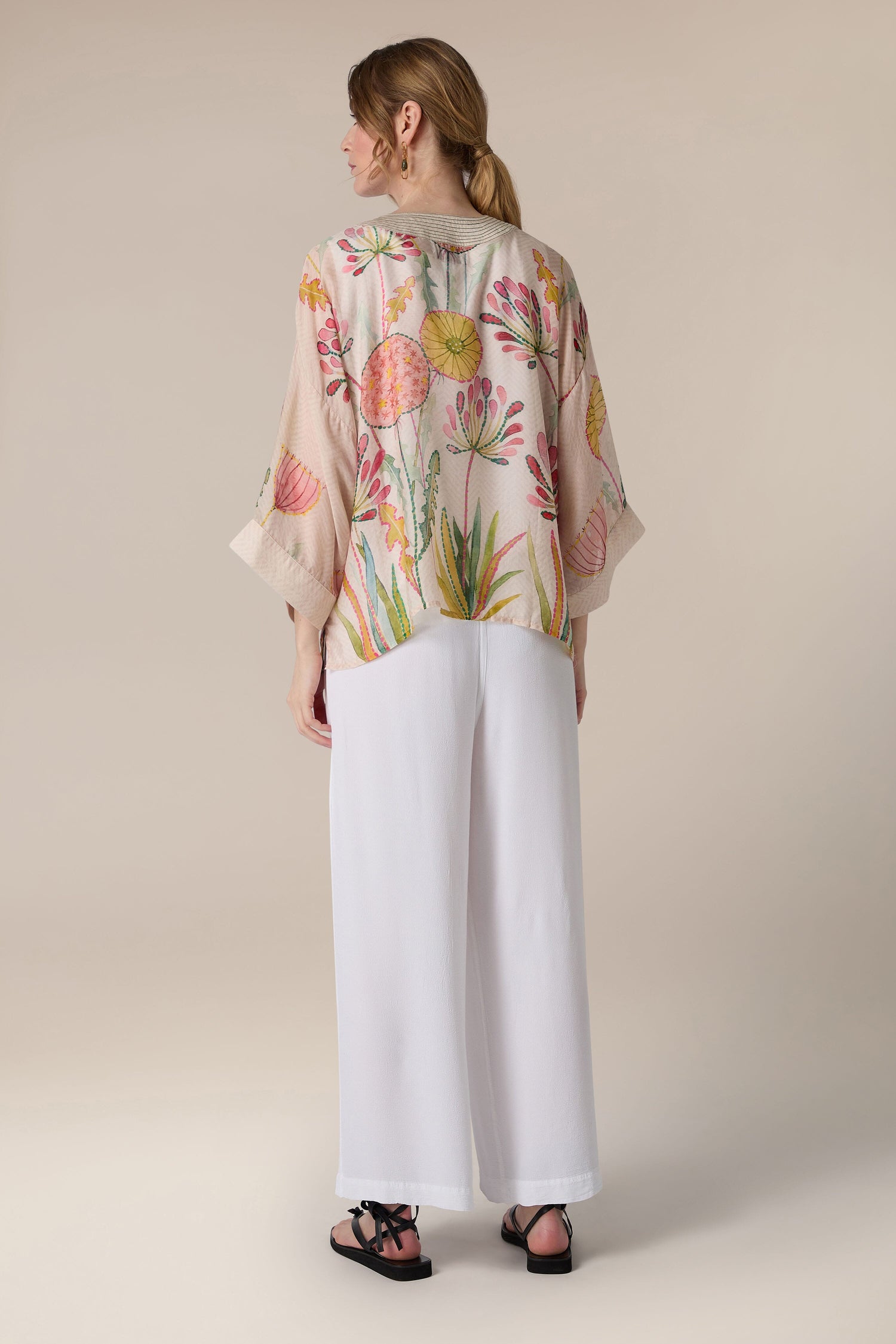 Woman standing with her back to the camera, wearing a Pop Flowers Kimono and white trousers.