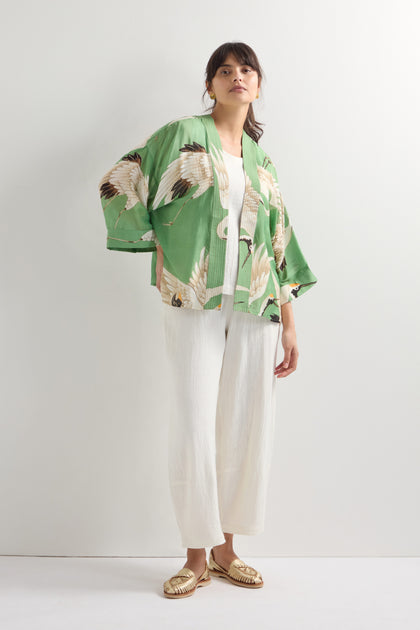 Someone is dressed in a Stork Print Kimono, along with a white top and pants, and gold sandals, standing against a plain light background.