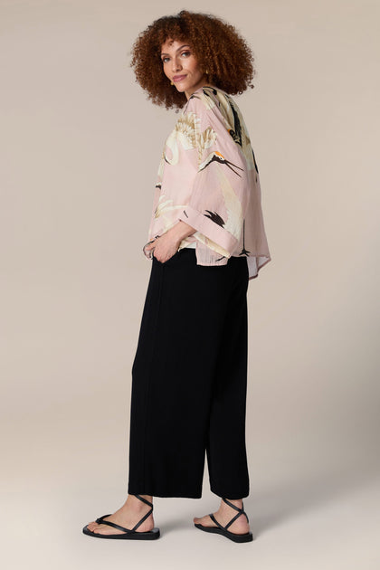 A woman wearing a pink blouse and black wide leg pants designed by Stork Kimono.