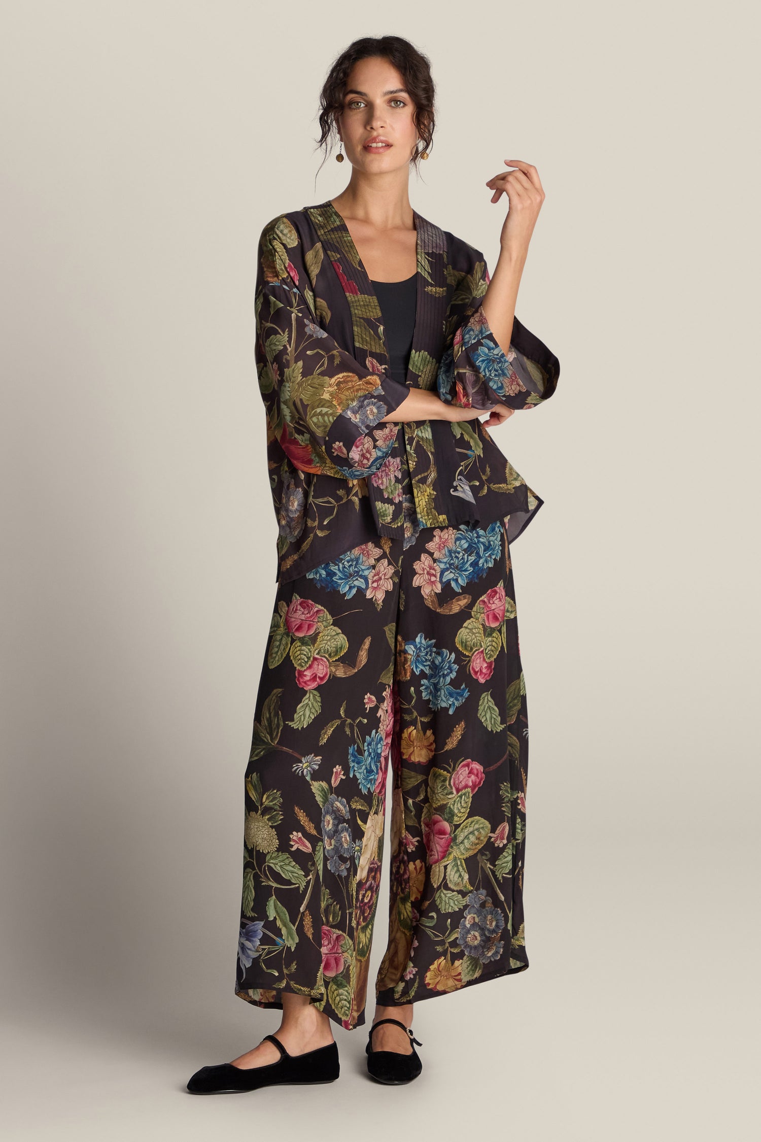 A person wearing the Primula Palazzo Trouser, featuring a vibrant painted floral print, and black flats stands prominently against a plain background.