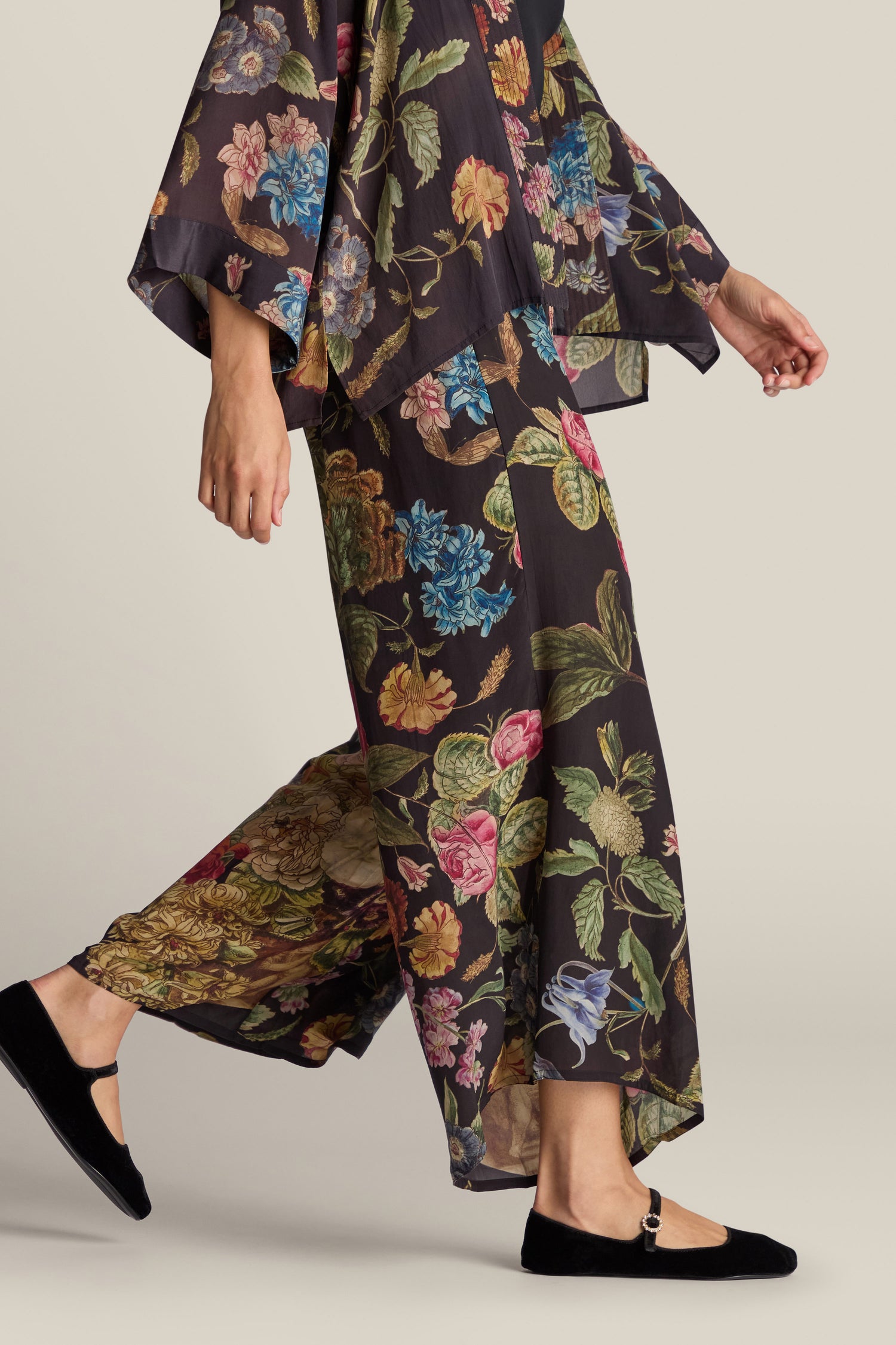 A person walks while wearing the Primula Palazzo Trouser, a floral-patterned outfit featuring wide-leg trousers and a loose-fitting top, paired with black flats.