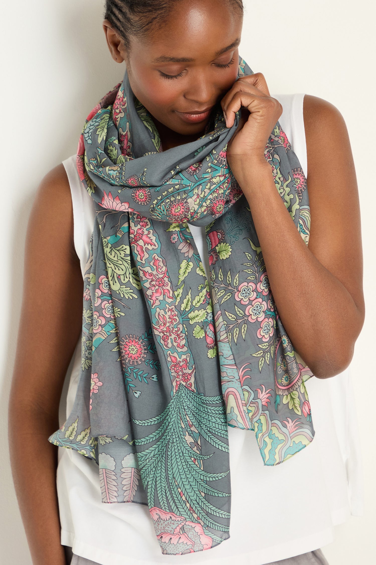 A woman in a white sleeveless top smiles while looking down, holding one end of the lightweight Boho Garden Print Scarf near her face.