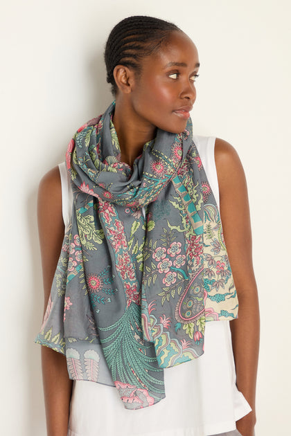 A woman in a sleeveless white top and the Boho Garden Print Scarf looks to the side against a plain background.