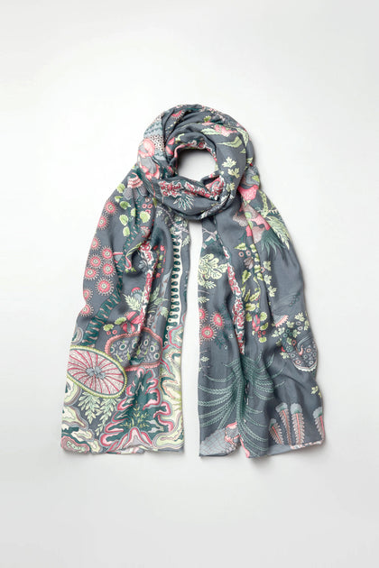 The Boho Garden Print Scarf features a dark base with floral and botanical patterns in green, pink, and cream, made from sustainable fabric and shown on a plain light background.