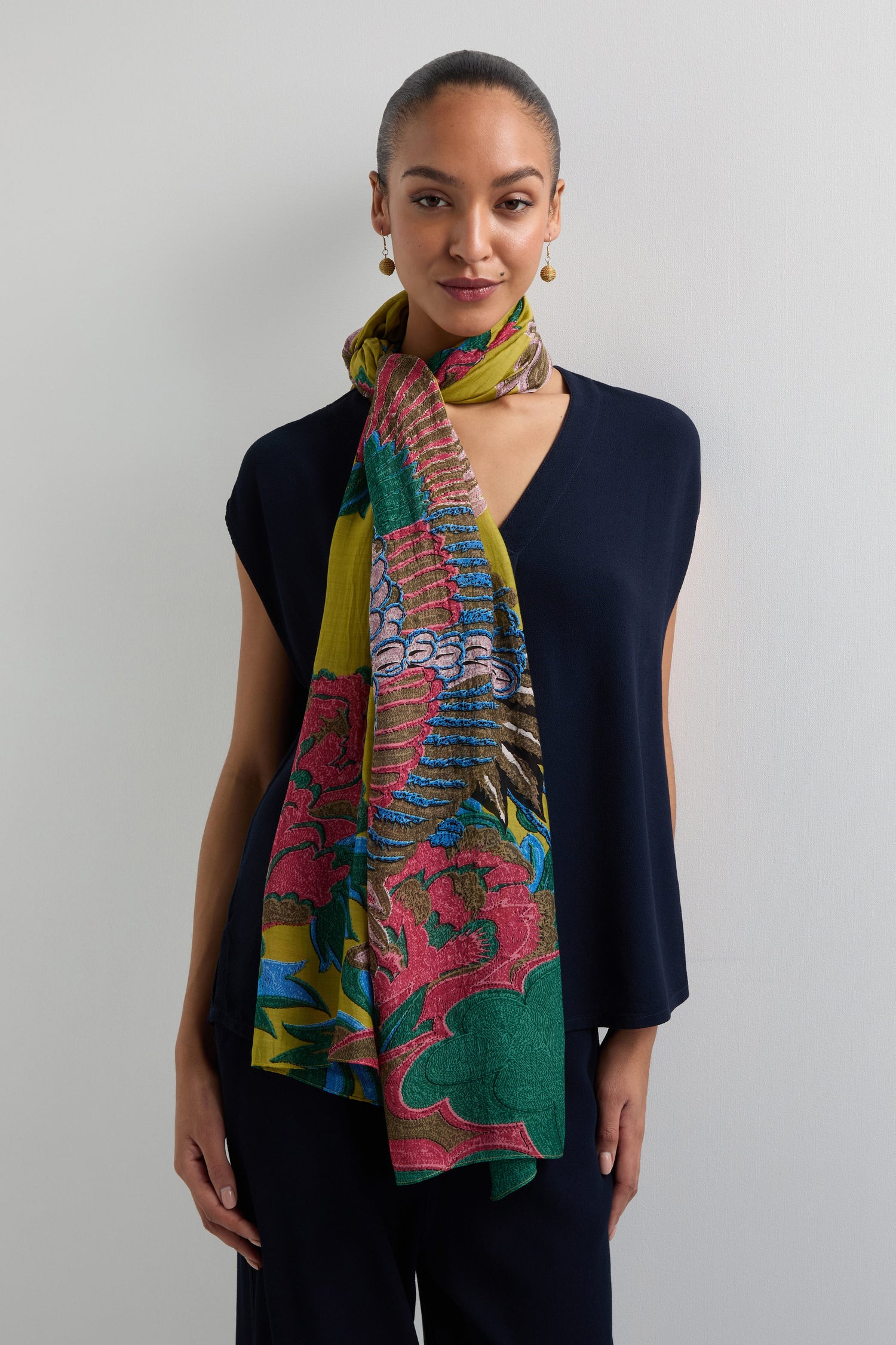 A person in a dark outfit pairs it with a Crane Print Scarf, featuring lively floral patterns similar to kimono designs, against a plain light background.