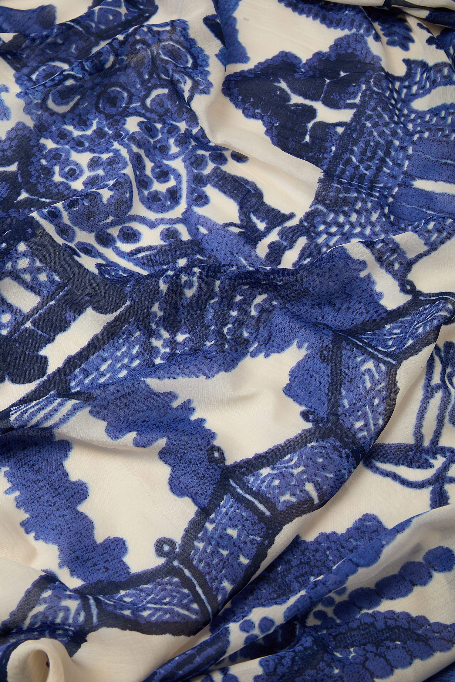 Close-up of a blue lace fabric pattern with the Willow Print Scarf elements on a beige background.