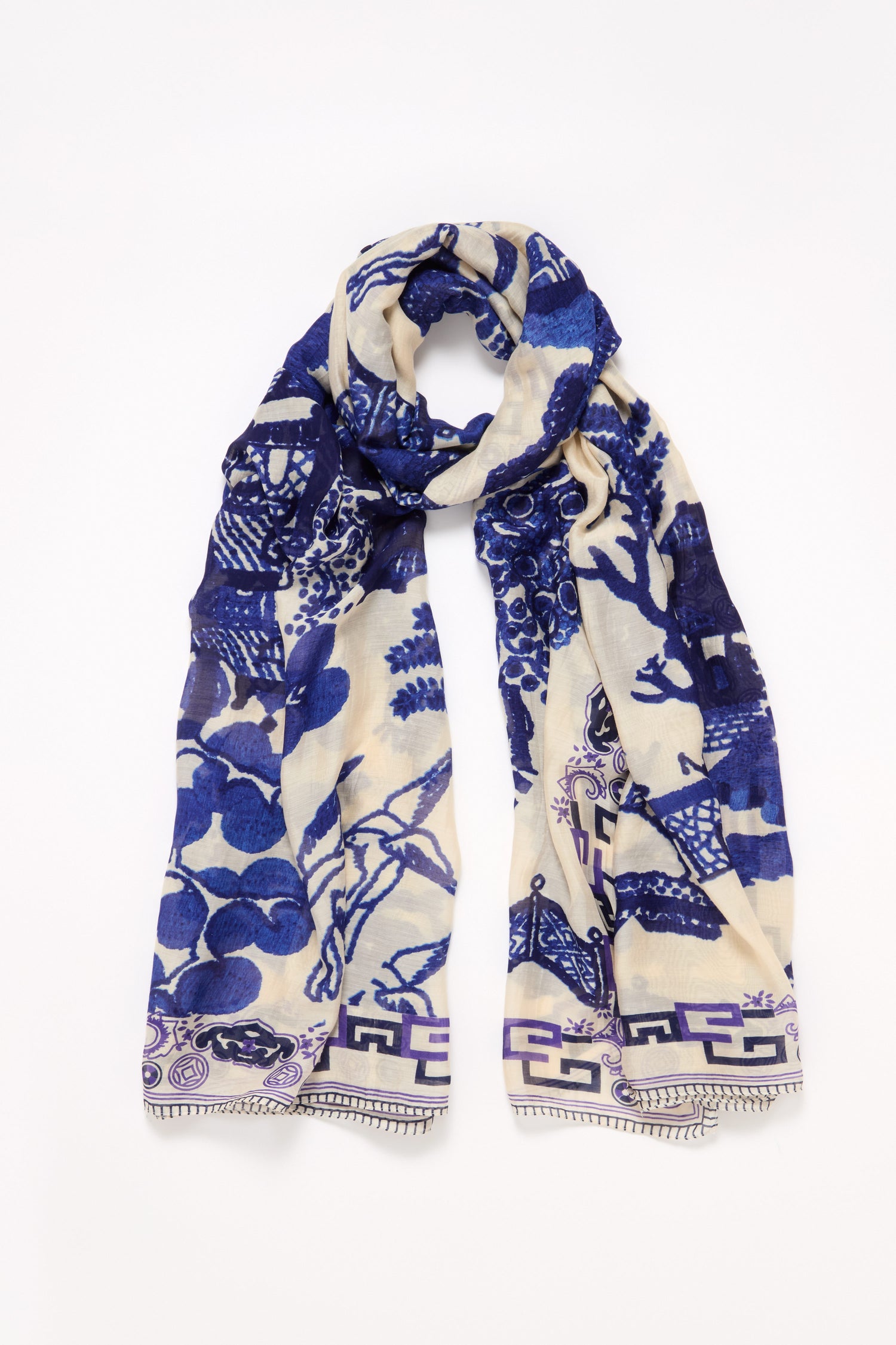 The Willow Print Scarf features a cream base with bold blue willow-inspired floral and geometric patterns, shown laid flat on a white background for a timeless and elegant look.