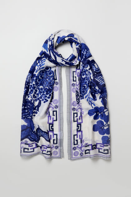 The Willow Print Scarf showcases blue floral and geometric patterns on white sustainable fabric, displayed flat against a light background.