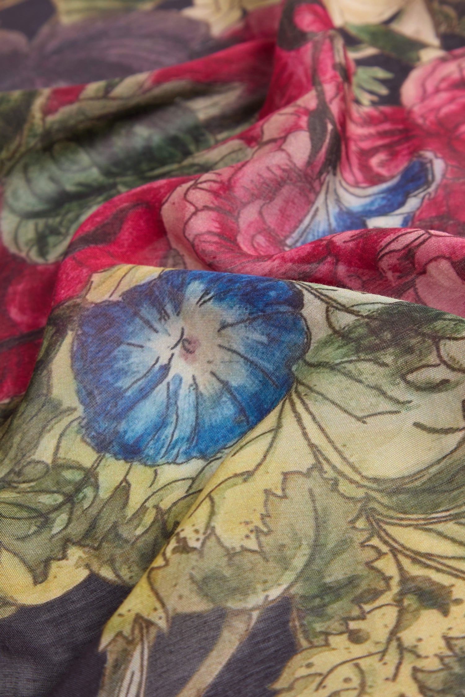 Close-up of the Primula Scarf, highlighting its floral print featuring blue, red, and green flower designs on a light, subtly sheer material—a stunning piece of sustainable fashion.