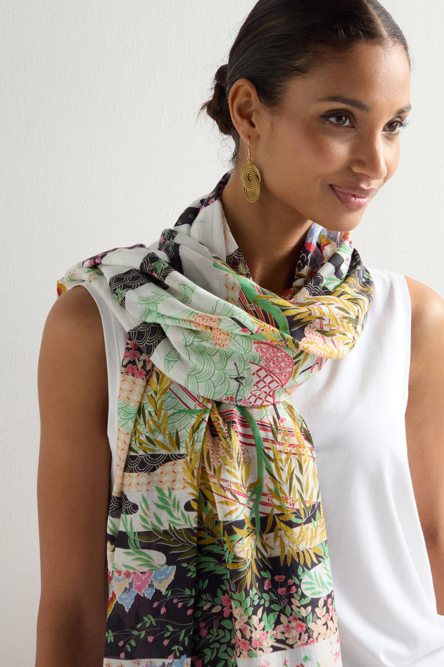 A woman in a white sleeveless top and the Spring Print Scarf showcasing Japanese landscapes, paired with gold earrings, stands against a light background.