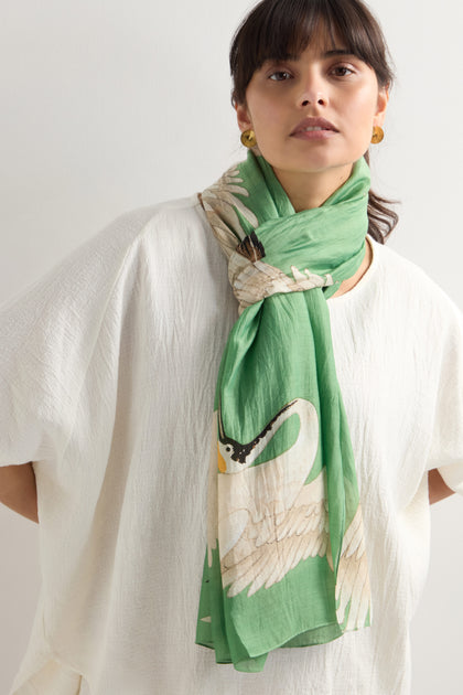 Person wearing a white shirt and the Stork Print Scarf, featuring an Art Deco-inspired green design with a swan motif.