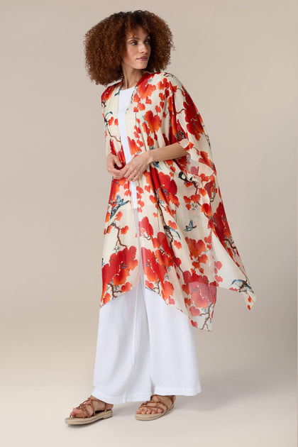 A woman in a red and white floral poncho, perfect for resort wear, resembling an Acer Throwover.