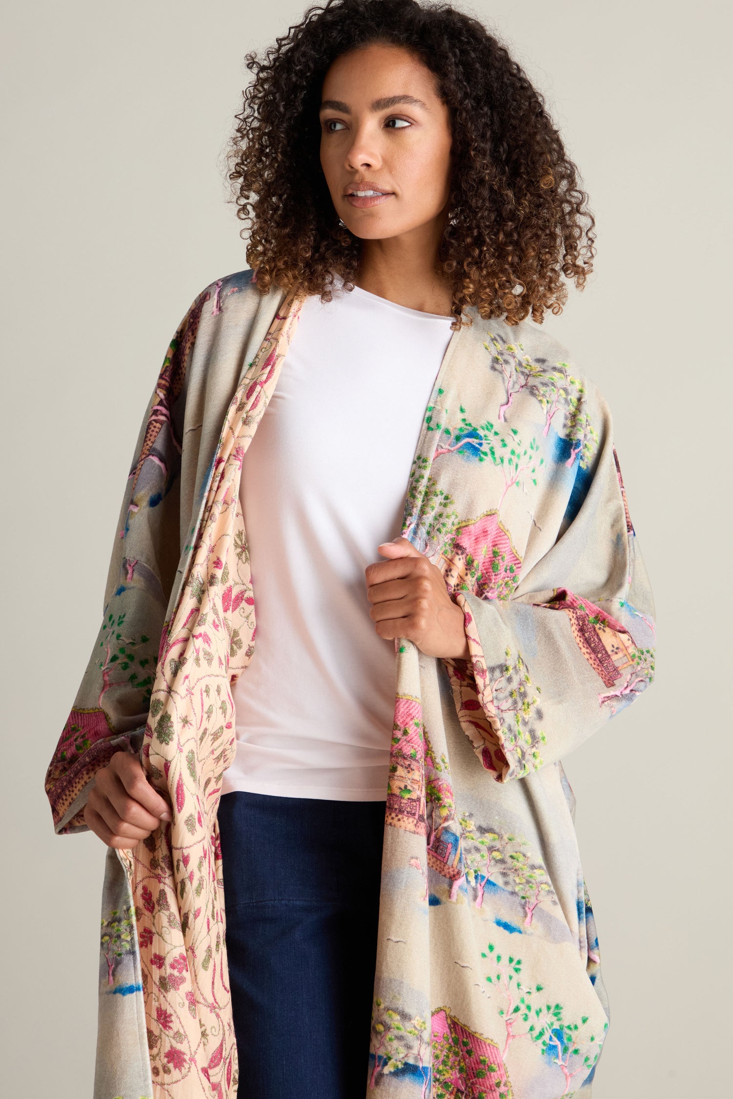 A woman with curly hair wears a luxurious Landscape Velvet Coat with a Japanese landscape print over a white shirt and blue jeans.