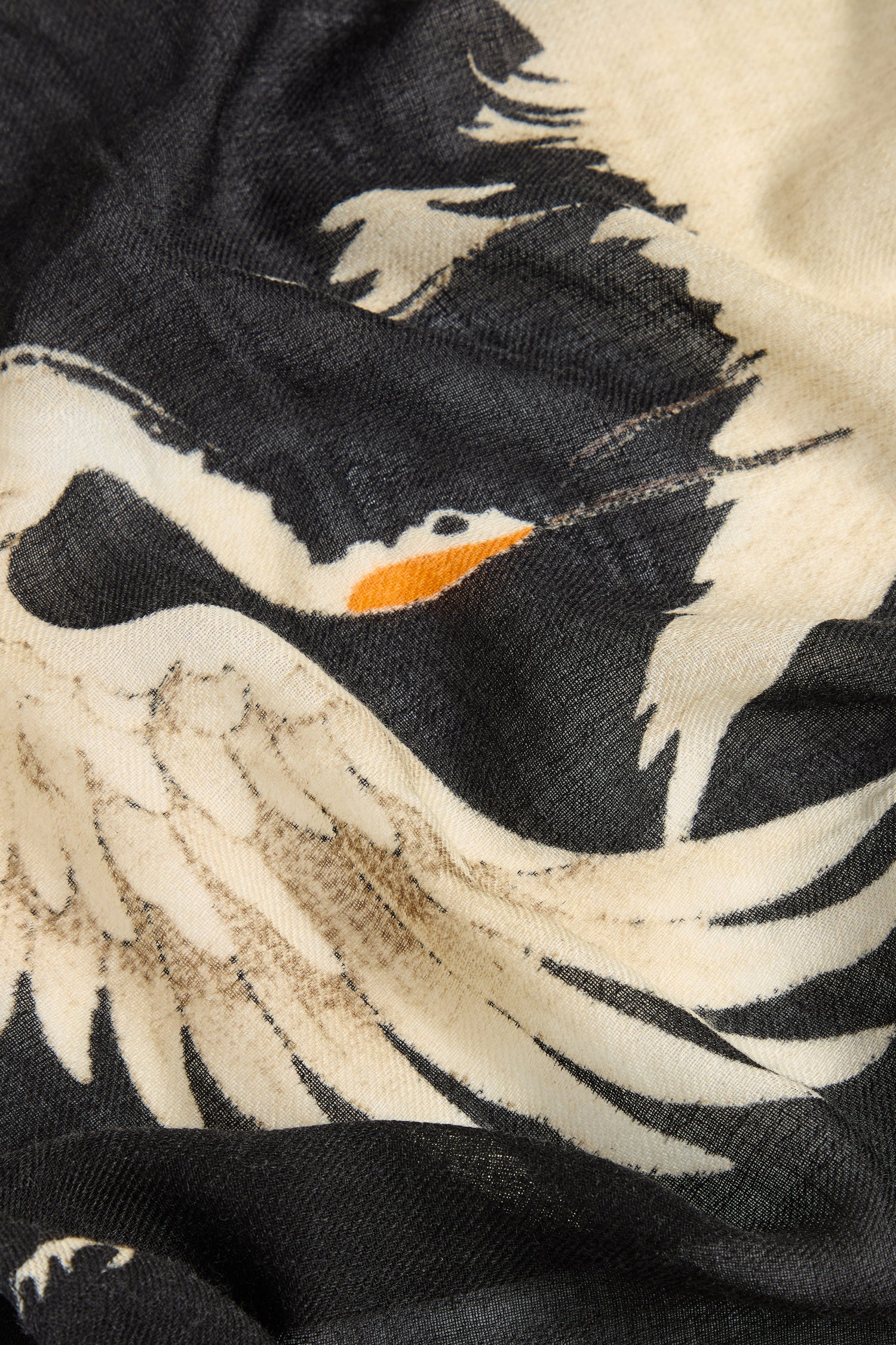 A close-up of the Stork Print Woollen Scarf, showcasing a black and white illustration of a crane with an orange beak in mid-flight, reminiscent of vintage-inspired luxury.