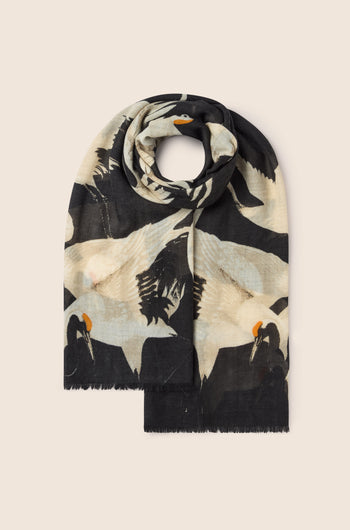 The "Stork Print Woollen Scarf," a vintage-inspired luxury accessory in black and beige, adorned with a pattern of cranes, is neatly folded against a plain background, exuding an Art Deco fashion charm.